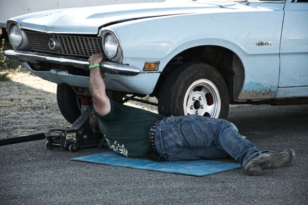 Man looking under broken car.